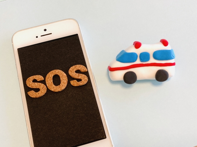 画面に「SOS」と書かれたスマートフォンと救急車のイラスト