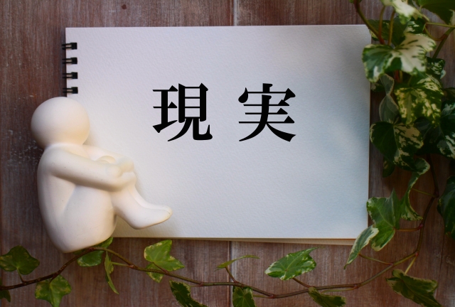 「現実」と書かれたメモ帳とうずくまる人形のイラスト