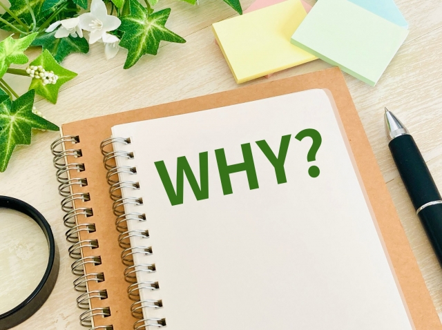 デスクの上のメモ帳に「WHY」と書かれたイラスト