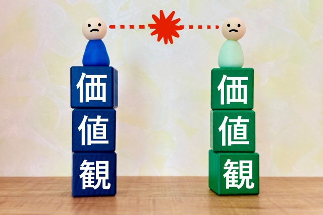 「価値観」と書かれた2つの積み木の上の2体の人形が火花を散らしているイラスト