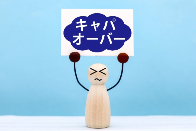 人形が「キャパオーバー」と書かれたボードを掲げているイラスト