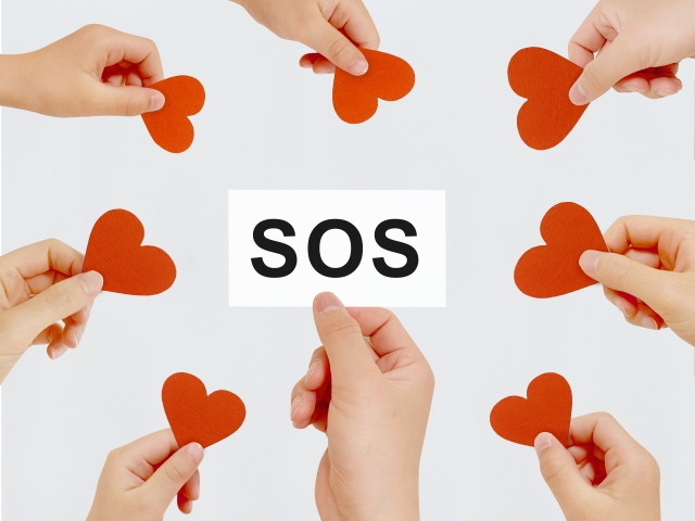 「SOS」と書かれたカードにハートマークが寄り添う画像