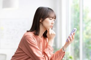 スマートフォンを見て考えごとをする女性の画像