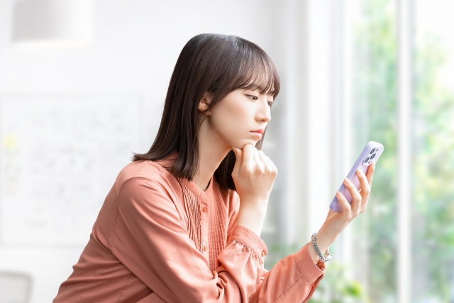 スマートフォンを見て考えごとをする女性の画像