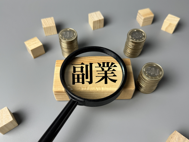 「副業」と書かれた木札と積まれた500円硬貨のイラスト