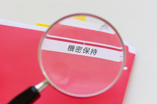 「機密保持」と書かれたファイルのラベルを虫眼鏡で覗いているイラスト